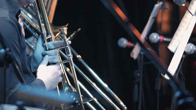 Close up of a musician playing trombone in a concert. Cool blue stage lighting reflects on the shiny brass instrument. Professional and focused mood for live jazz or classical orchestra events