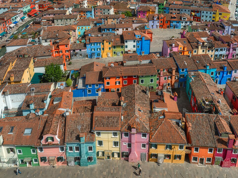 Aerial view of a vibrant patchwork of houses with terracotta roofs creates a stunning mosaic of color against the blue sky, Burano, Veneto, Italy.