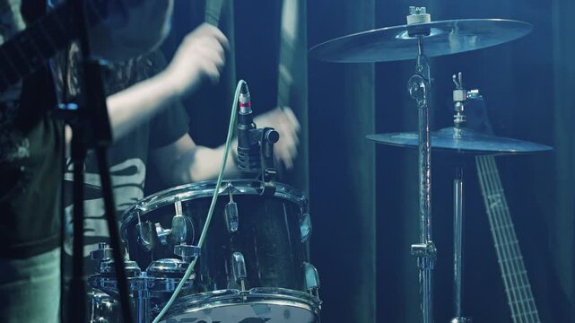 A drummer plays a drum kit during a live rock concert or rehearsal. Close-up on the snare drum, microphone, and cymbals under moody stage lighting. Concept of live music, energy, and performance