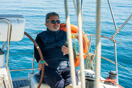 Mature man navigating sailboat steering wheel on blue sea