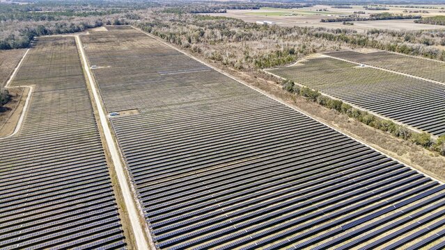 Aerial view of vast solar panel arrays stretching across the landscape under a clear sky, juxtaposed with patches of bare earth, Elkton, Florida, United States.