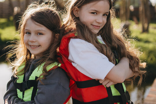 Two young girls in life jackets smile happily near water on sunny day showing fun summer adventure