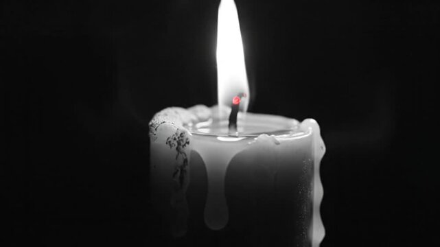 Burning candle wick with flame and drifting wisps of smoke in a darkened room, dramatic lighting.