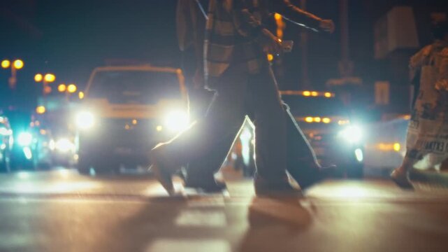 Groups of pedestrians navigate a busy city street at night, surrounded by glowing streetlights and moving vehicles. The energy of urban life is palpable as they cross