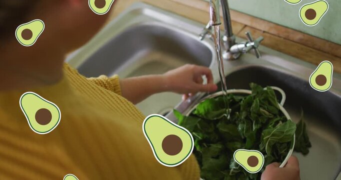Animation of avocado icons falling over caucasian woman rinsing salad