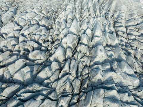 Aerial view of the glacial ice field, etched with deep crevasses and shadowed patterns, creates a stark, textured landscape, Fjallsarlon, Sveitarfelagid Hornafjordur, Iceland.