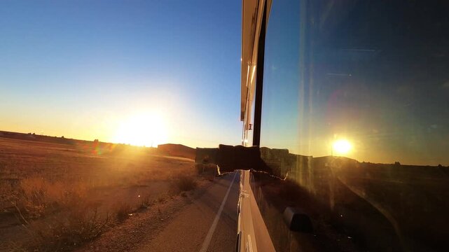 Comfortable travel with woman sitting in camper passenger seat at sunset, enjoying journey. Exterior front perspective with road motion, countryside nature and soft summer evening light