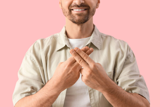 Adult man using sign language on pink background, closeup