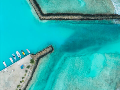Aerial view of boats moored at the pier, contrasting with the vibrant turquoise waters and dark breakwaters creating a striking visual harmony, Vashafaru Island, Maldives.