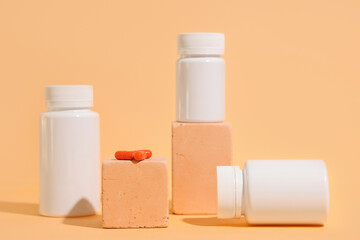 Decorative podiums with blank plastic vitamin bottles and pills on orange background