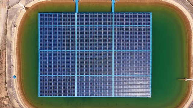 Floating photovoltaic farm covering an irrigation reservoir viewed from directly above, surrounded by green water and earthen banks