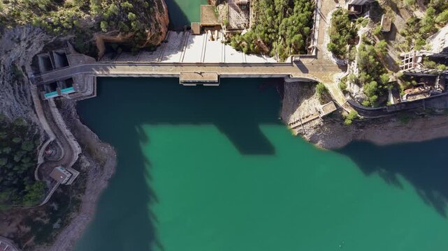 Overhead view of Benageber dam spanning the turquoise Turia River in Valencia, Spain, surrounded by rocky canyon walls and pine forest