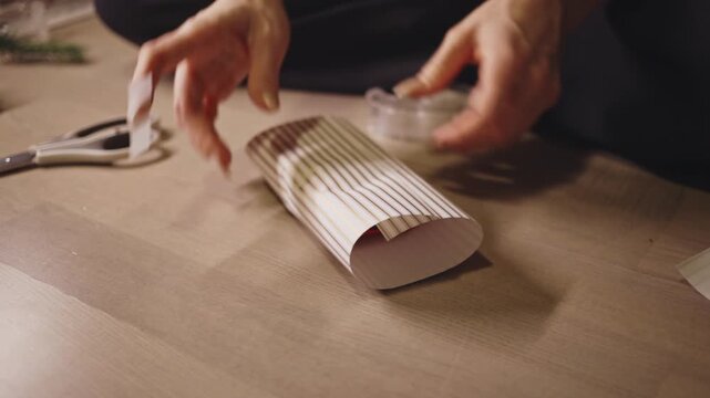 Wrapping Christmas Gift With Striped Paper And Sealing With Scotch Tape. - closeup shot