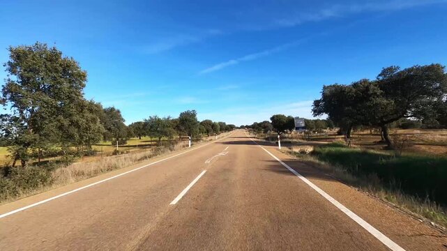 Endless asphalt road perspective stretching through countryside under summer sun, symbol of distance and life journey. POV of vehicle moving forward toward unknown destination with blue sky and open h