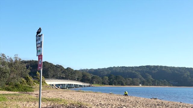 Sandy beach with coastal bridge and signpost in foreground, Tathra, New South Wales, Australia.