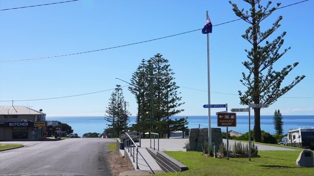 Small coastal town street leading toward ocean with trees and signage, Tathra, New South Wales, Australia.