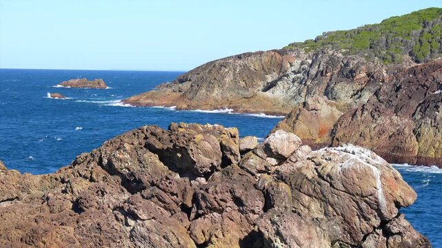 Rocky headland in foreground with coastal cliffs and ocean beyond, Tathra, New South Wales, Australia.