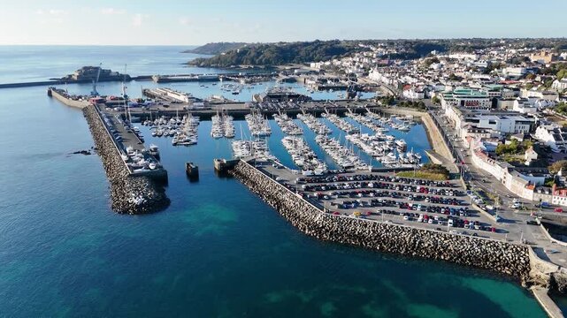 St Peter Port Guernsey backwards drone flight over QEII Marina and Salerie corner with backdrop of Castle Cornet and harbour with stunning deep blue calm clear sea in late afternoon sun