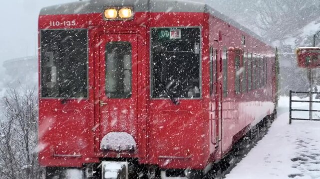 Beautiful red train driving into station in rural Japanese snow countryside