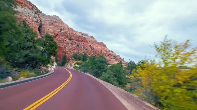 Scenic footage from a moving vehicle captures the beautiful landscape of the Zion-Mount Carmel Highway in Zion National Park, Utah. Towering reddish sandstone cliffs and sparse green vegetation line t