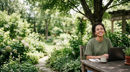 Fototapeta premium Smiling Hispanic woman working on laptop at wooden table in a lush garden backyard.