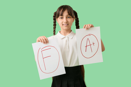 Happy schoolgirl holding papers with grades on green background