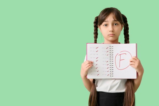 Sad schoolgirl holding notebook with bad results of school test on green background