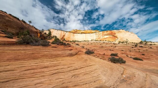 A wide-angle shot capturing the stunning, rugged landscape of Zion National Park in Utah, USA. The foreground features textured, wavy red rock formations, leading the eye towards massive, towering san