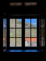 Fototapeta premium View from a dark room through a wooden-framed window onto a green hill