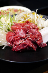 Fototapeta premium Fresh raw beef bulgogi with assorted vegetables including green onions, bean sprouts, and enoki mushrooms on a black plate, traditional Korean marinated beef preparation before cooking