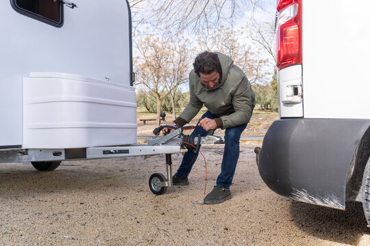 Man preparing to tow a trailer or caravan, adjusting the hitch connection to a motorhome or van for a journey