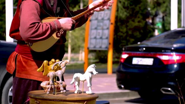 Kazakh street musician playing dombra with moving puppet toys, traditional culture performance