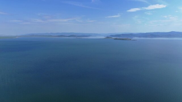 Majestic aerial drone footage showcasing the vast deep blue water surface of the Bukhtarma Reservoir in East Kazakhstan. Crystal clear water and bright sunny weather highlight the immense scale 