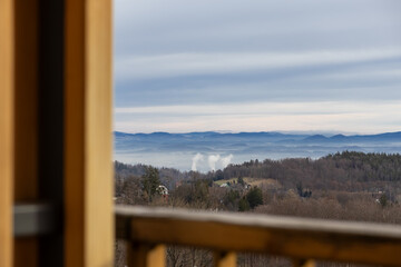 Fototapeta premium Serene panoramic misty mountain landscape featuring layered blue hills and bare forest trees, framed by a rustic wooden balcony, embodying peaceful nature scenery