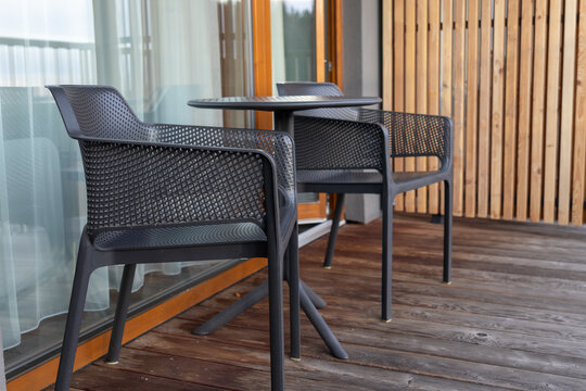 Two modern black chairs with a matching round table are set on a wooden balcony deck, providing a comfortable outdoor seating area for relaxation and leisure