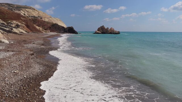 Aerial drone view of waves washing onto a pebble beach with Aphrodite's Rock in the background in Cyprus