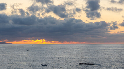 Naklejka premium Colorful sunrise over the Cantabrian Sea with a traditional Basque rowing boat training near the coast of San Sebastian in the Basque Country, Spain.