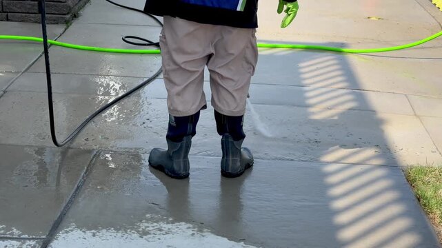 Man with rubber boots power washing concrete sidewalk