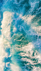 Vertical top-down view of turquoise ocean water with powerful white sea foam and bubbles. A dynamic and refreshing nature scene capturing the energy of the waves.