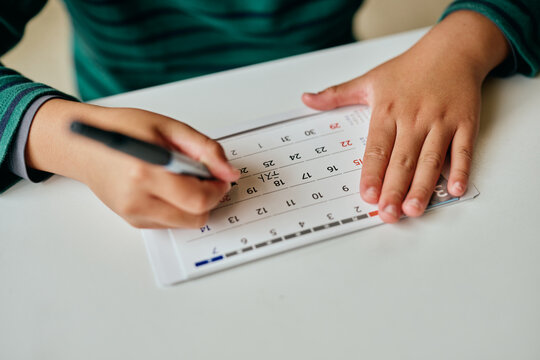 Asian elementary school student marking test date on calendar at home
