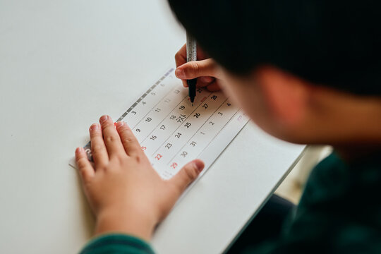 Asian elementary school student marking test date on calendar at home