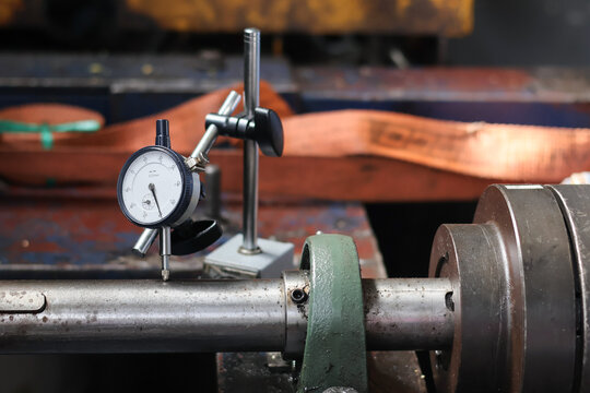 Mechanical engineer using dial indicator gauge to measure shaft runout and alignment on industrial machine in workshop
