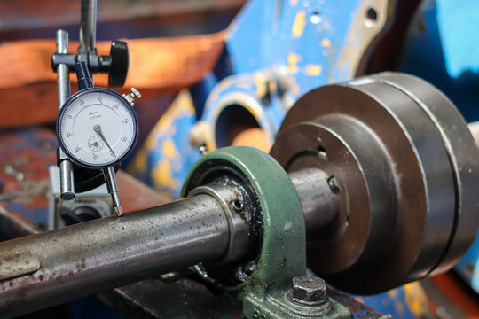 Dial test indicator measuring shaft runout on industrial machinery in a workshop. Precision tool checking mechanical rotation accuracy on steel metal part.