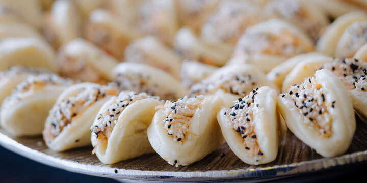 A close-up of a tray of bite-sized pastries filled with shredded filling and topped with sesame seeds, ideal for a buffet or party.
