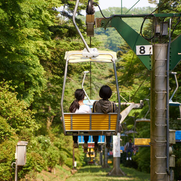 Mother and daughter riding a chairlift down a mountain surrounded by lush greenery.