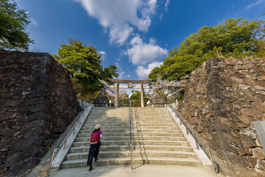 Woman with red backpack walking up stone stairs toward Takeda Shrine torii gate