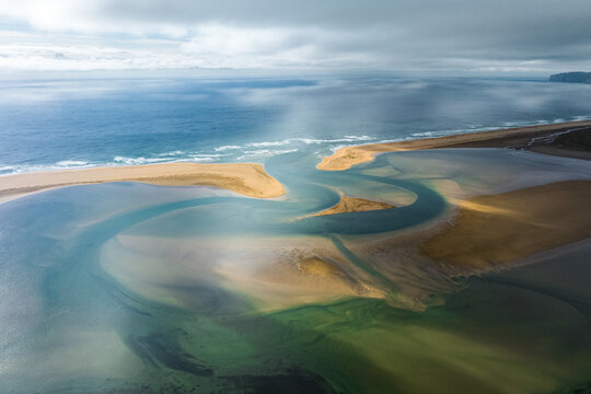 Aerial view of winding waterways meet the North Atlantic ocean on a cloudy day, Raudisandur, Iceland.