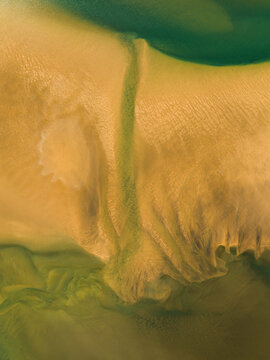 Aerial view of winding waterways carve through the ochre sand, blending into the surrounding emerald green vegetation, Raudisandur, Vesturbyggd, Iceland.