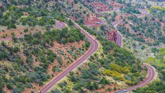 A high-angle, wide shot of the iconic, winding Zion-Mount Carmel Highway (Route 9) switchbacks as they descend into the canyon, viewed from the scenic Canyon Overlook Trail in Zion National Park, Utah