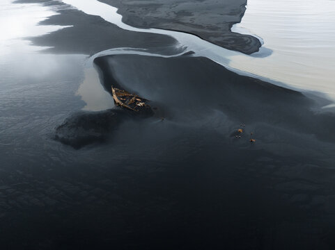 Aerial view of a stranded boat resting on the black sands where glacial rivers meet, creating a stark contrast of textures and tones, Skaftafell, Iceland.